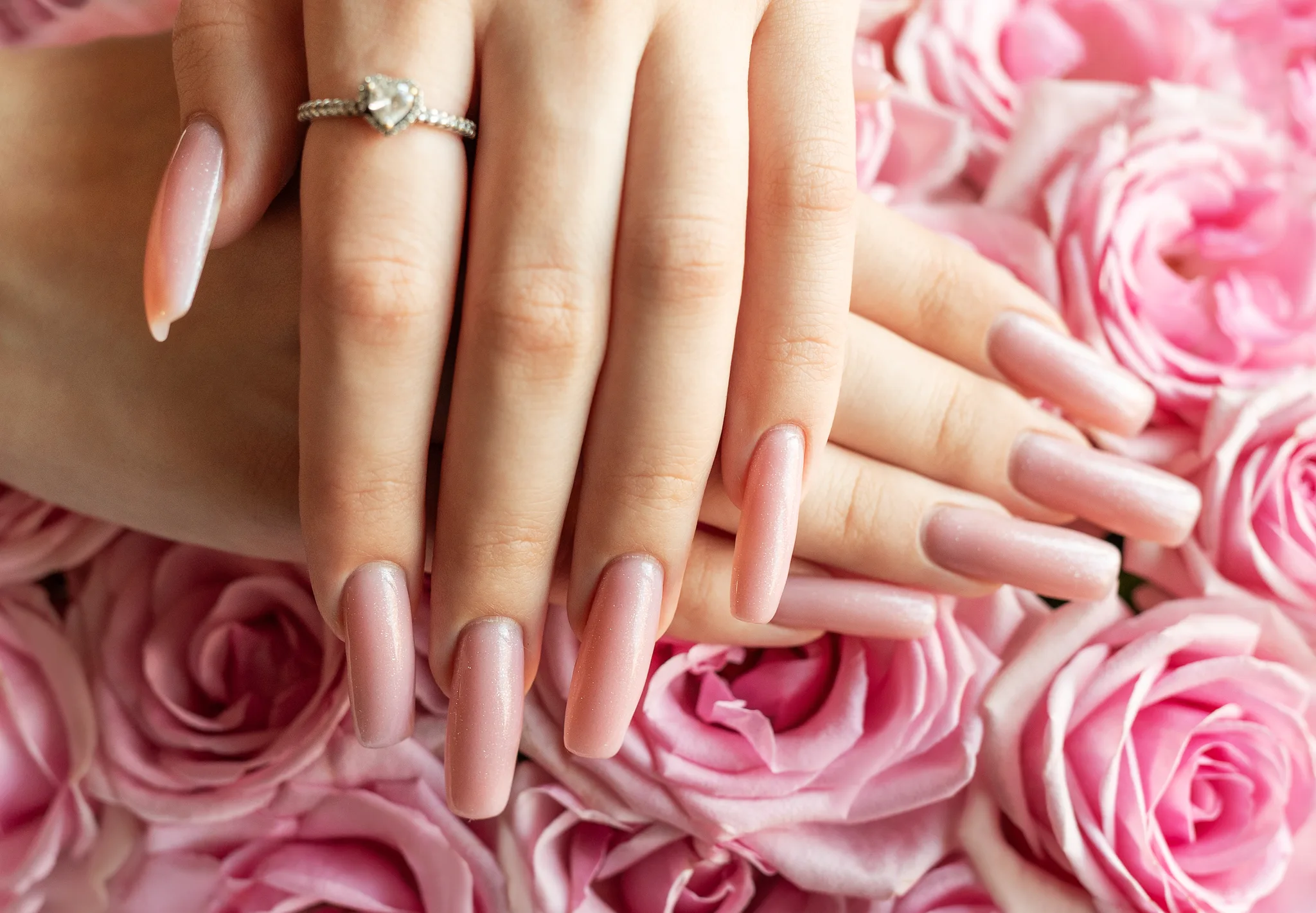 a hand with an engagement ring over pink roses